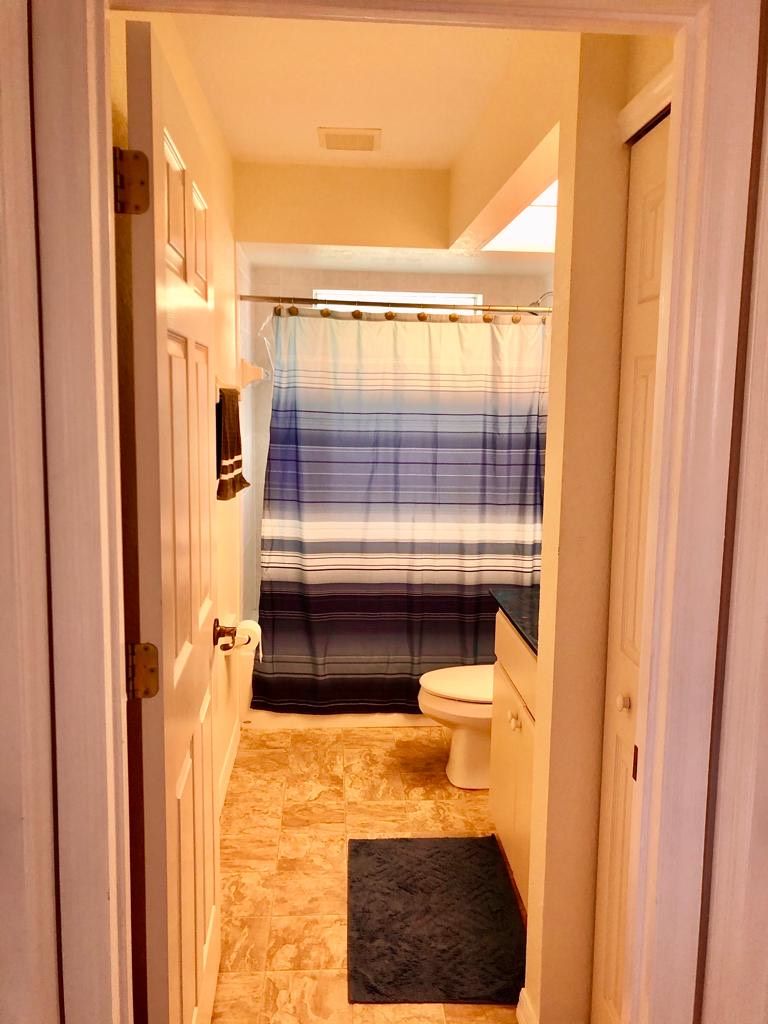A narrow bathroom with a striped shower curtain, a toilet, and a small rug on the floor.