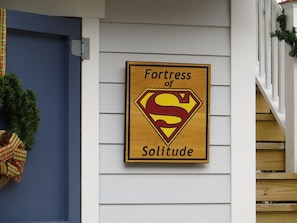 A wooden sign with a Superman logo and the words "Fortress of Solitude" on a house wall.