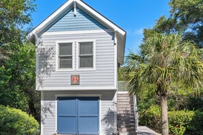 A two-story house with a blue garage door, a small porch with a white railing, and a sign that reads 'Fortress of Solitude.'