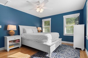 Une chambre à coucher avec un lit, des tables de chevet, un ventilateur de plafond et une fenêtre avec des stores.