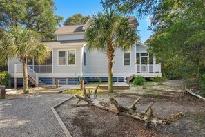 A two-story house with a porch, surrounded by trees and a wooden deck. - Four bedroom home with private crofter located in the heart of the island close to amenities. (Bald Head Island)