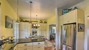 Cucina con isola centrale, mobili bianchi, elettrodomestici in acciaio inossidabile e illuminazione a sospensione.