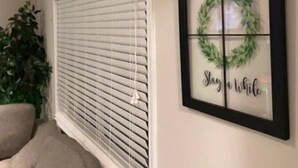 A room with a window with blinds, a framed picture with a wreath and the words "Stay a while", and a potted plant. - Sale!!! Emerald Grande family home (Atlanta)