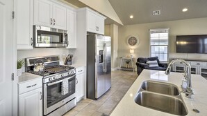 A modern kitchen with white cabinetry, stainless steel appliances, a large island with a sink, and a flat-screen TV mounted above the island. - Washington Townhome w/ Patio + Resort Perks! (Washington)