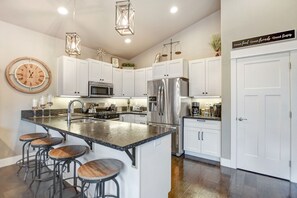 A modern kitchen with white cabinets, stainless steel appliances, a central island with stools, and pendant lighting. - The Sleepy Canoe -  A Cozy River front house near everything in Southern Oregon (Gold Hill)