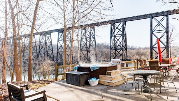 An outdoor deck with a hot tub, seating area, and a view of a bridge. - Riverfront hidden gem, ground floor open space! (Madison Heights)