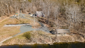 A two-story house with a large porch, surrounded by a wooded area and a small pond. - Riverfront hidden gem, ground floor open space! (Madison Heights)