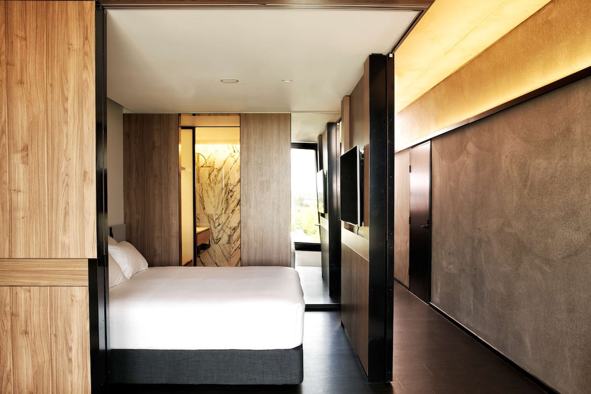 A modern hotel room with a large bed, a TV mounted on the wall, and a view of the outdoors.