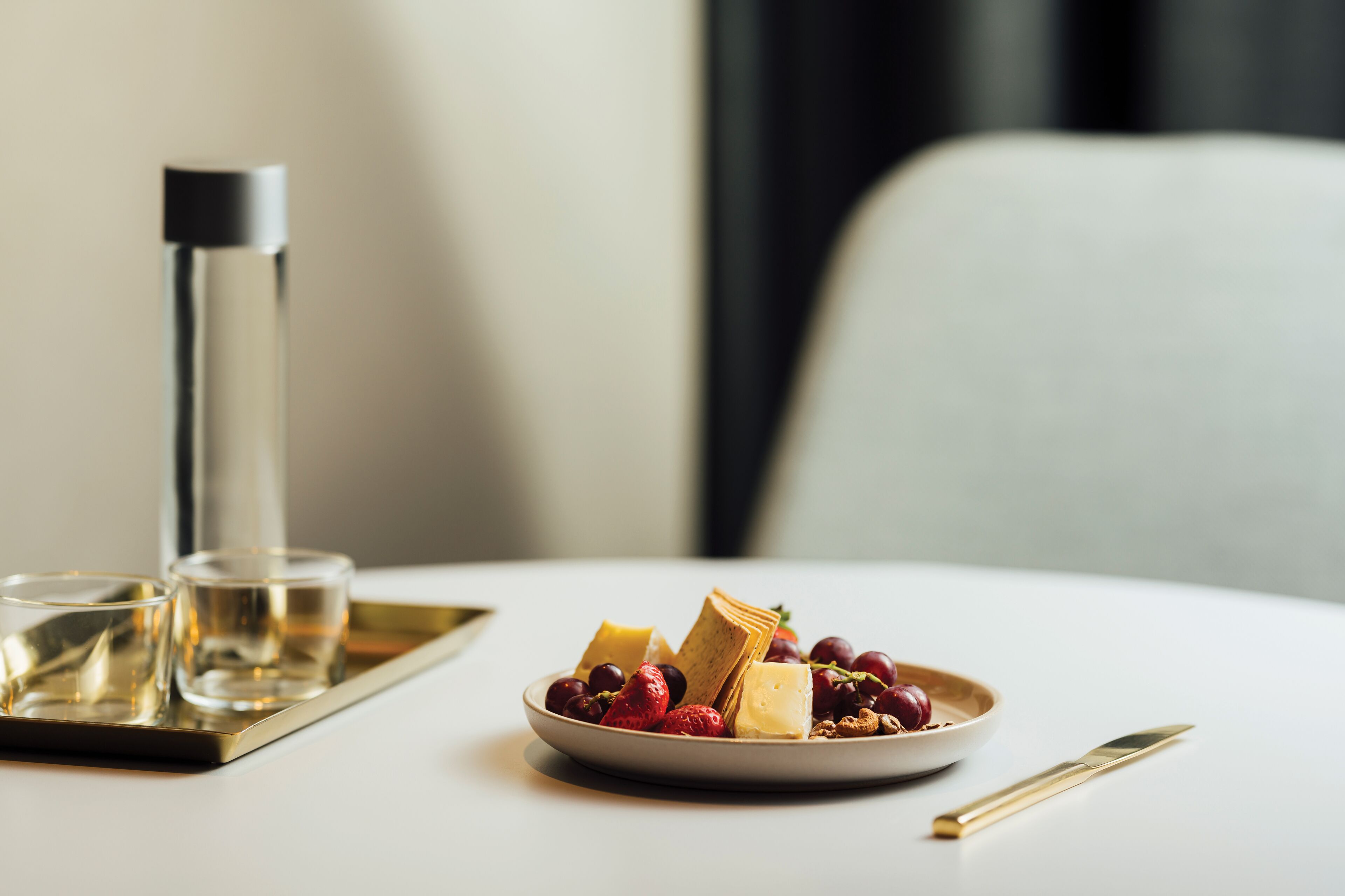 Una mesa de comedor con un plato de queso, uvas y fresas, un vaso de agua y un cuchillo.