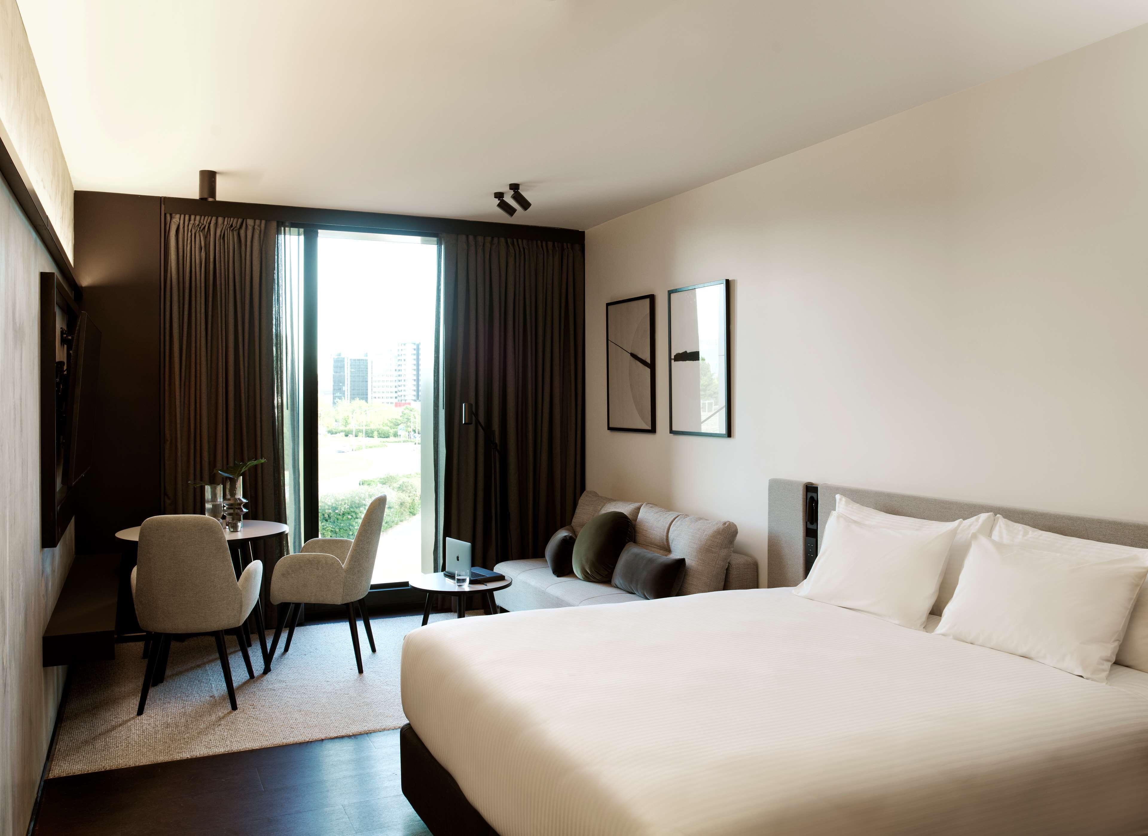 Habitación de hotel con una cama grande, un escritorio con una silla, una mesita y vistas a la ciudad a través de la ventana.