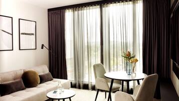 Una sala moderna con un sofá, dos sillones, una mesita redonda y un amplio ventanal con cortinas.