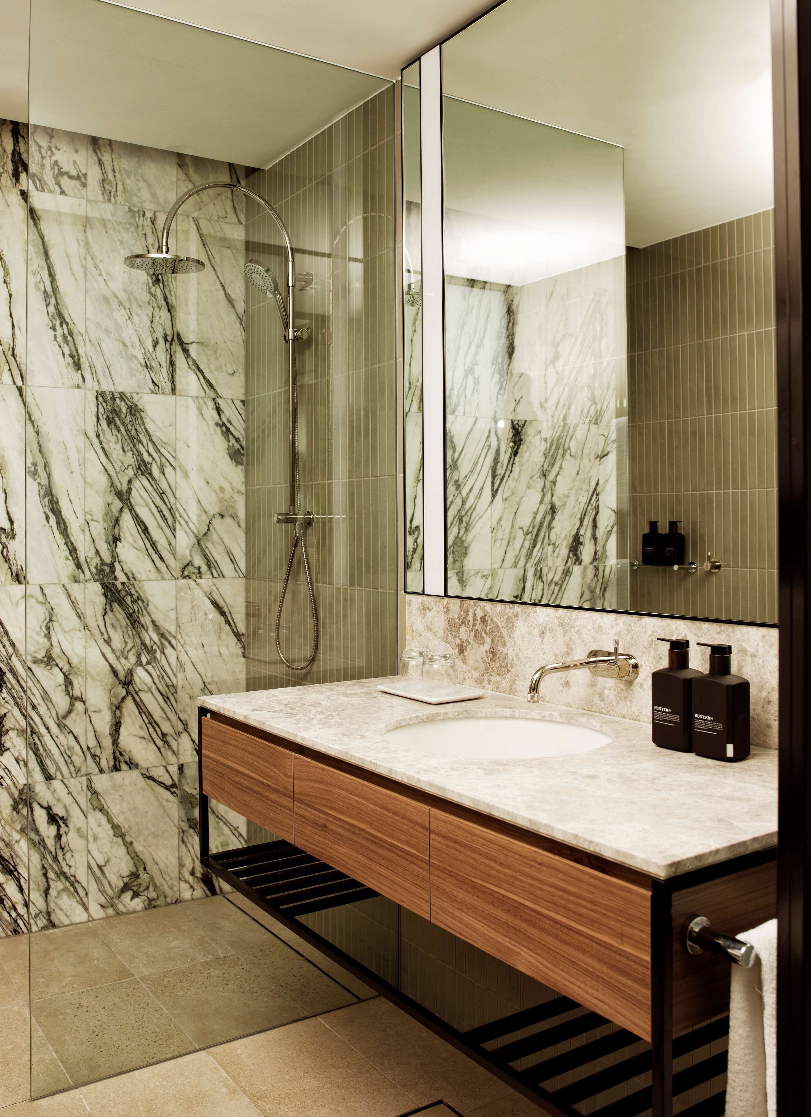 Un baño moderno con ducha de mármol, un espejo grande y un tocador de madera con lavabo.