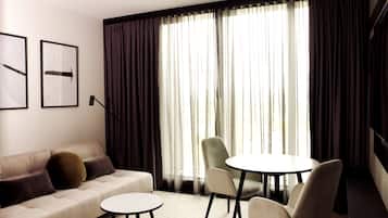 Ein modernes Wohnzimmer mit einer Couch, zwei Sesseln, einem kleinen runden Tisch und einem großen Fenster mit Vorhängen.