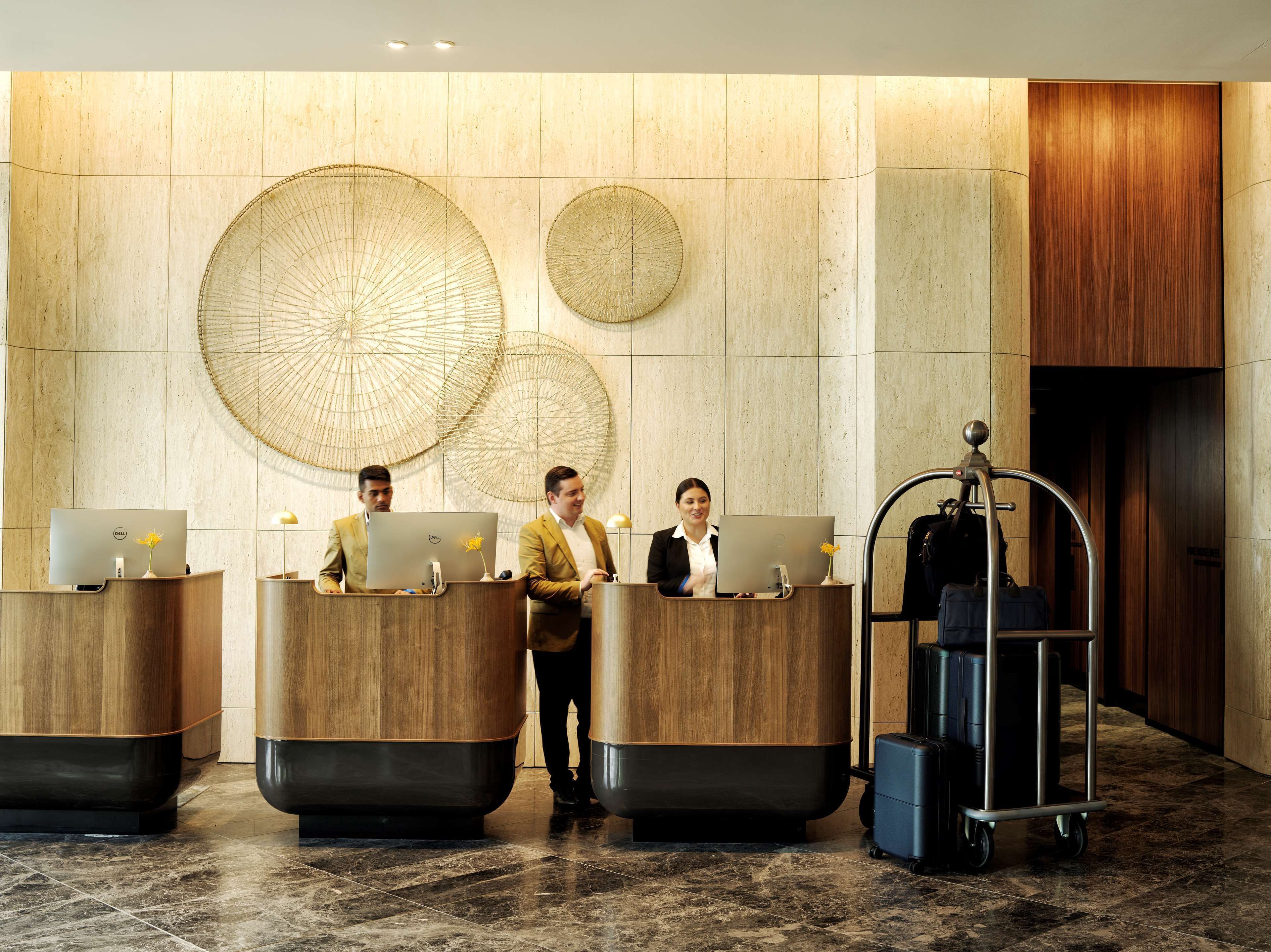 A reception area with three receptionists at desks, a luggage cart, and decorative wall art.