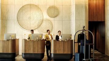 A reception area with three receptionists at desks, a luggage cart, and decorative wall art.
