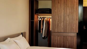 Quarto de hotel com uma cama grande, um guarda-roupa e um cabideiro com diversas peças de roupa.