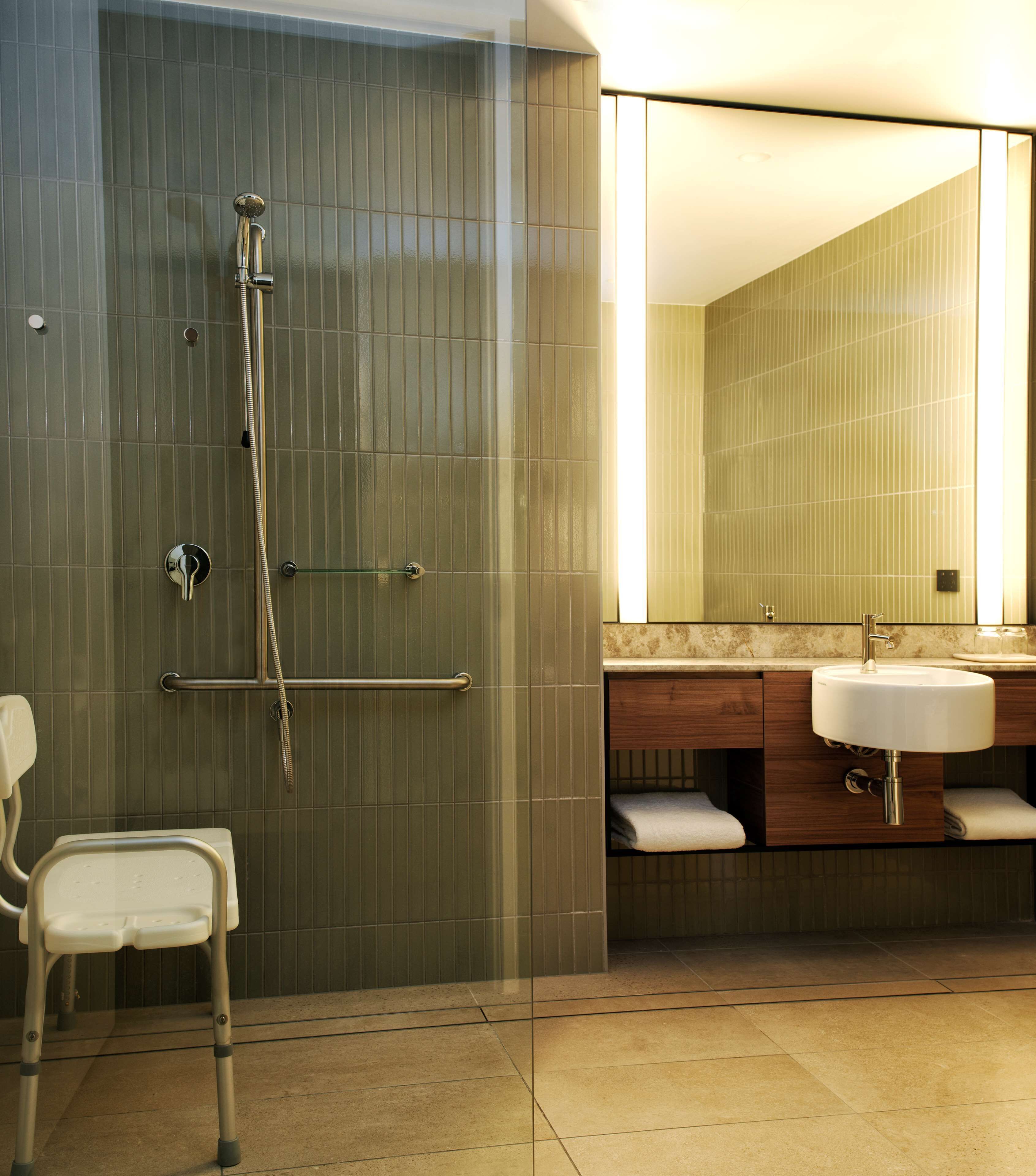 A modern bathroom with a glass shower enclosure, a white chair, and a vanity with two sinks.