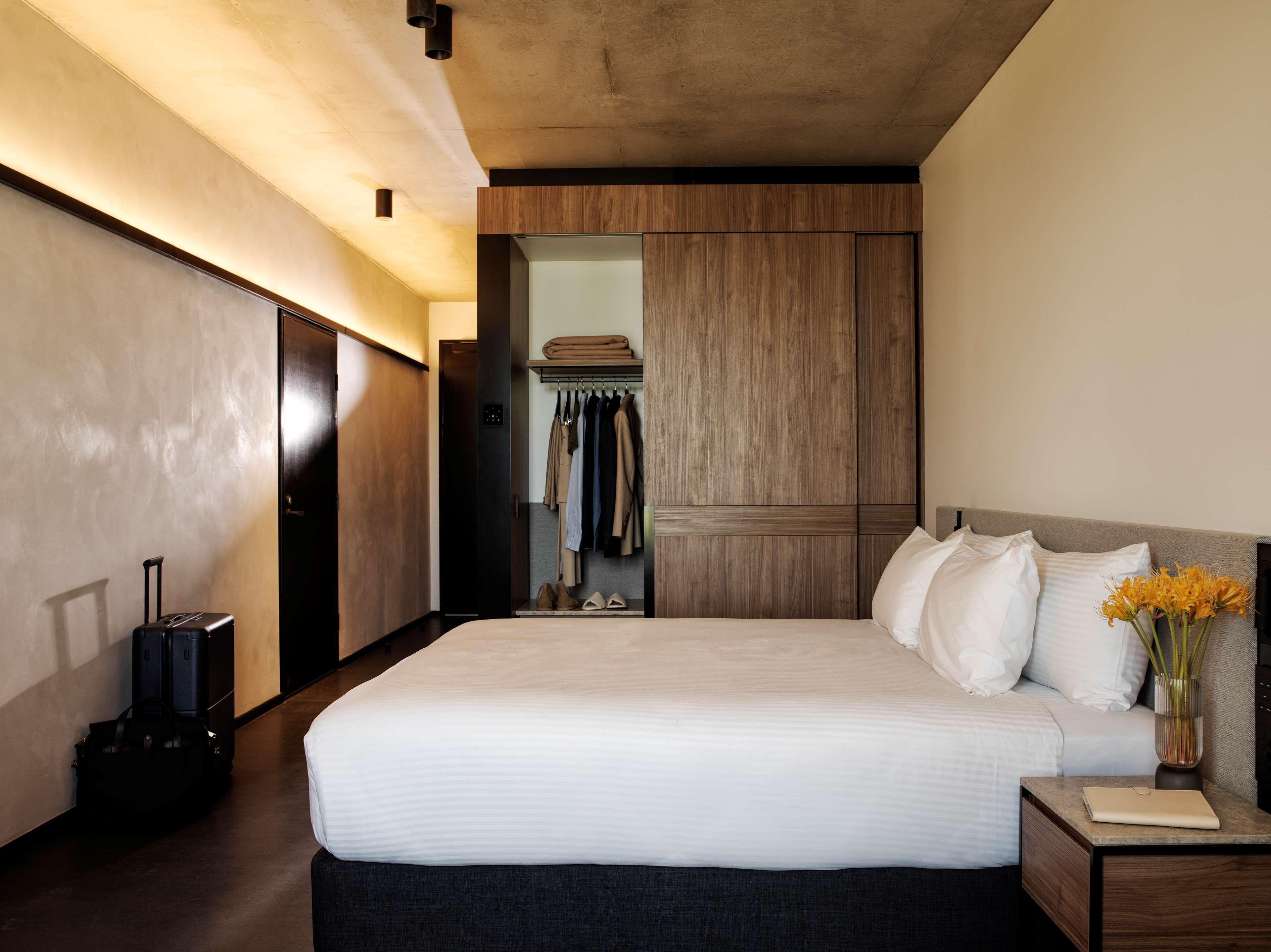 Une chambre d’hôtel moderne avec un grand lit, une table de chevet, une valise et une armoire.