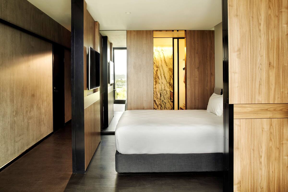 A modern hotel room with a large bed, wooden paneling, a TV, and a view of the outdoors.