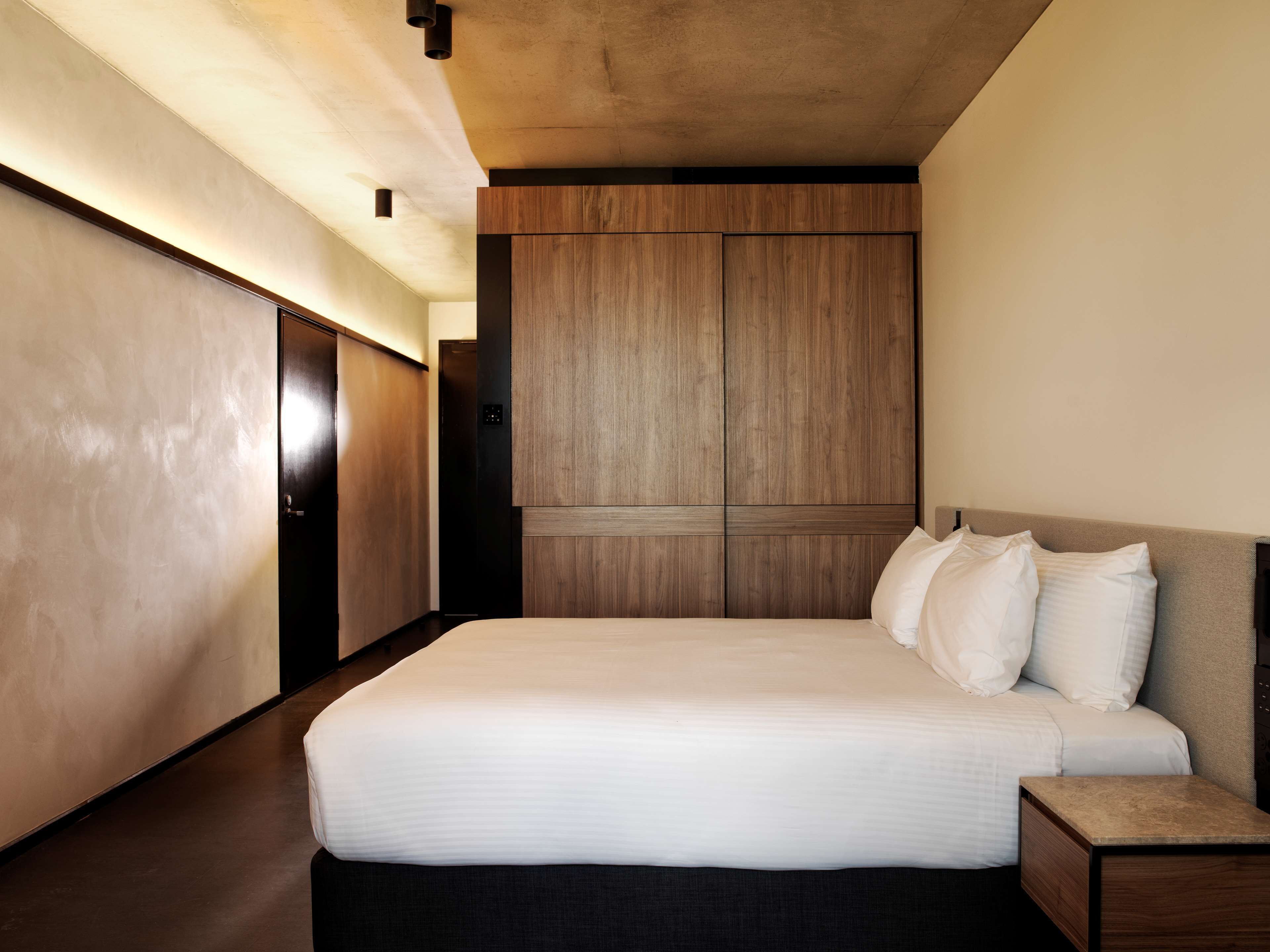 A modern hotel room with a large bed, wooden wardrobe, and a nightstand.