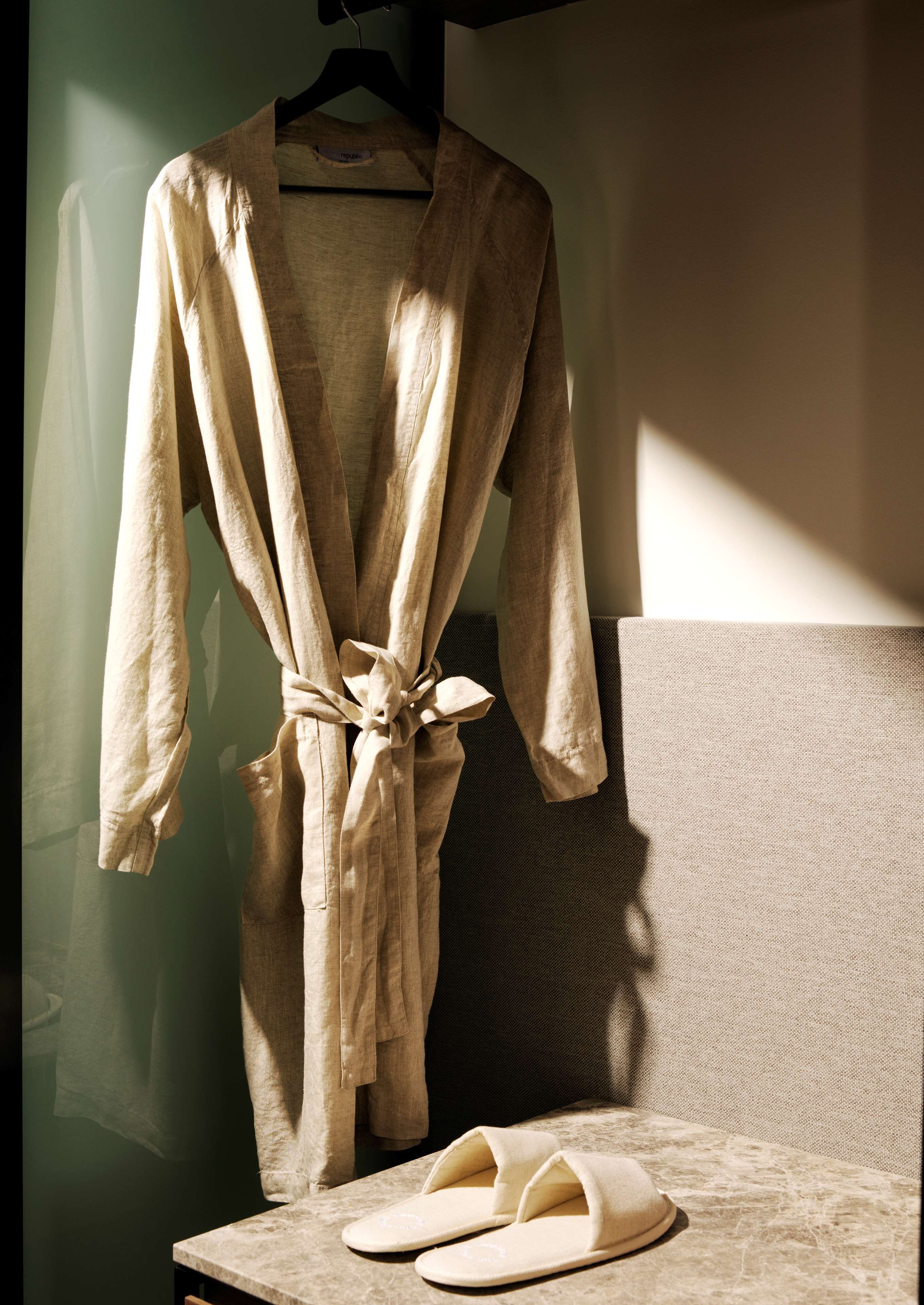 A robe hanging on a rack with slippers on a table.