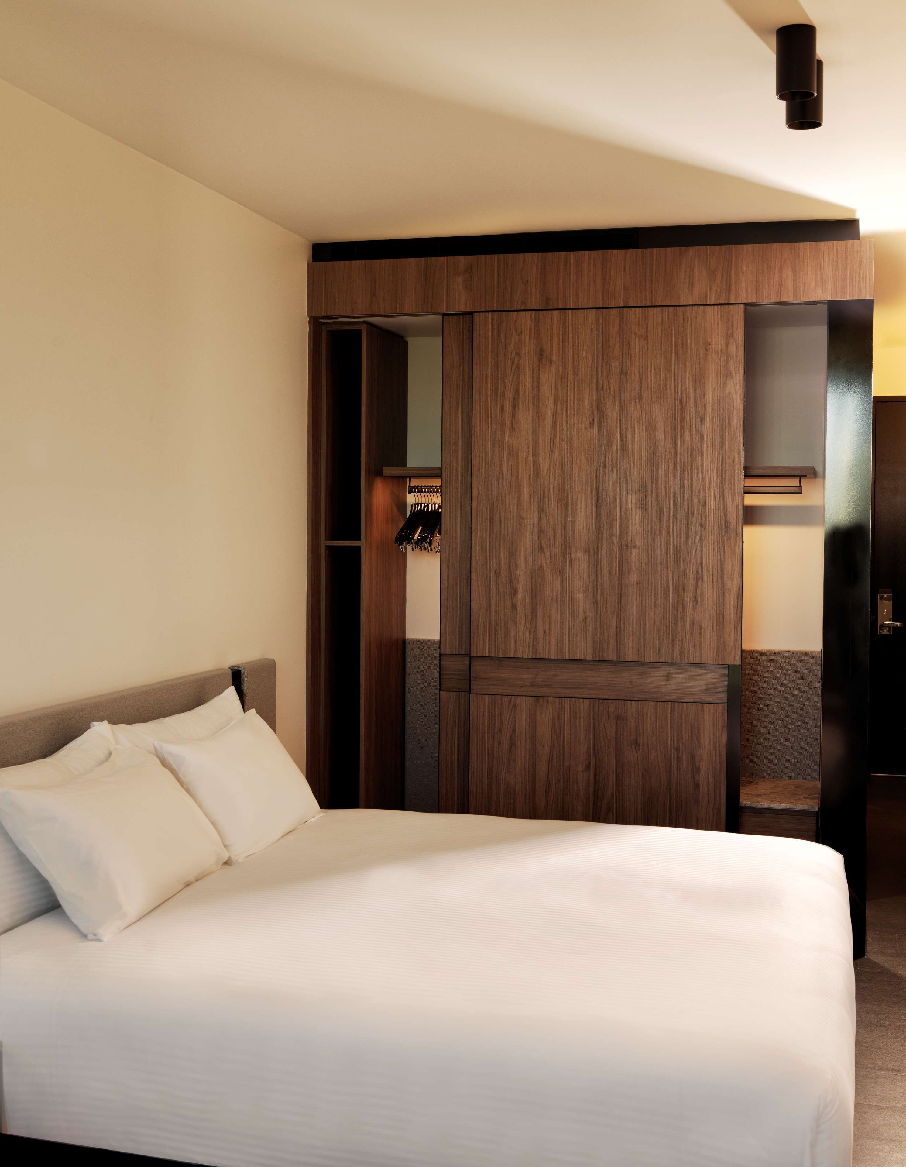 A hotel room with a large bed, wooden wardrobe, and a built-in closet with hanging space.