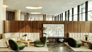 Un hall d’entrée moderne avec un plafond haut, une grande œuvre d’art abstraite et un espace détente comprenant des canapés et des fauteuils.