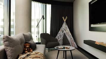 A modern living room with a sofa, a small round table, a television, a large window with curtains, and a decorative teepee.
