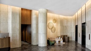 A modern lobby with a reception desk, a green armchair, a round coffee table, and a large pillar. - A by Adina Canberra (Canberra)