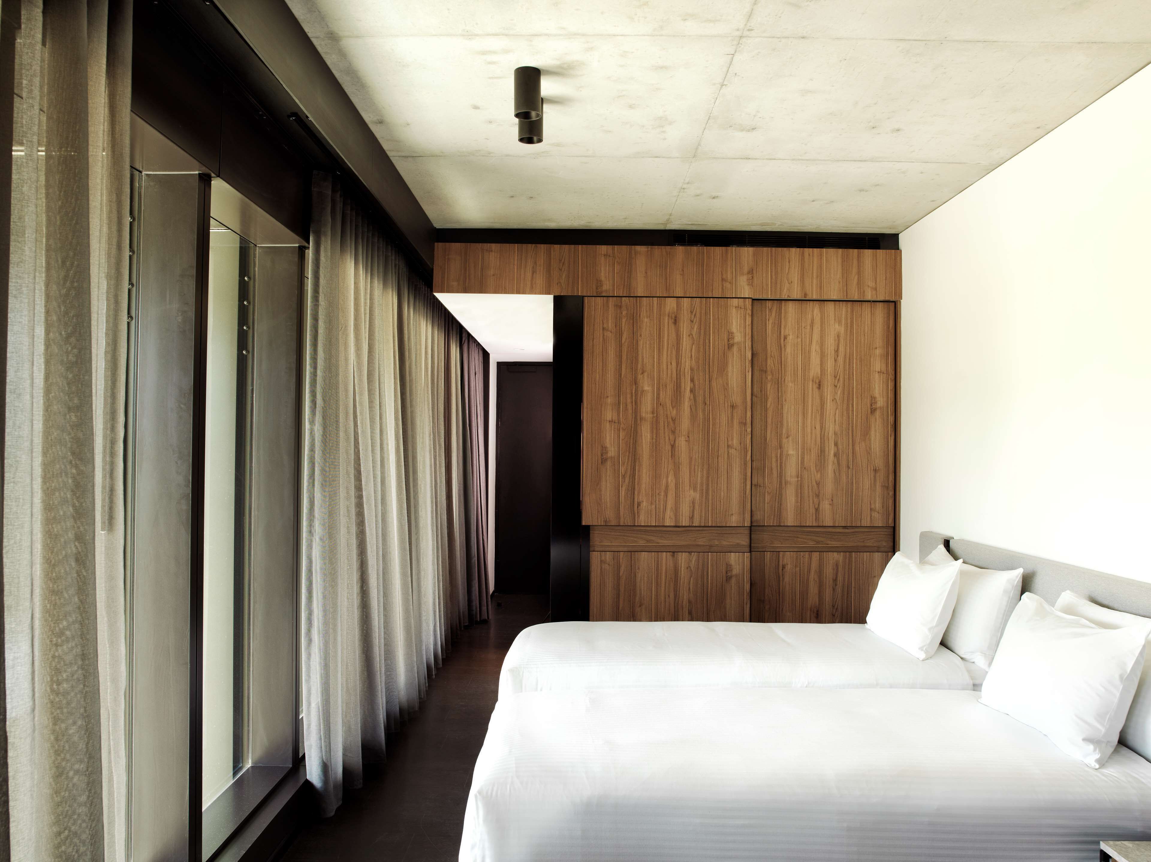 A hotel room with a large bed, curtains, a wooden panel wall, and a ceiling light.