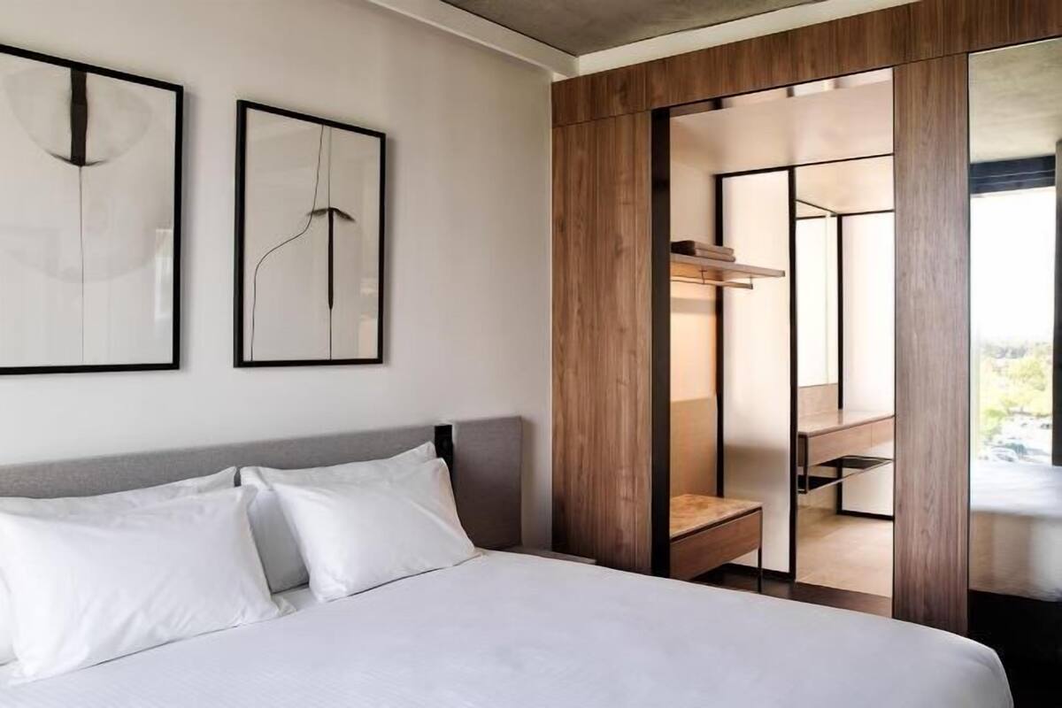 A modern hotel room with a bed, two framed artworks, a wooden wardrobe, and a view of a balcony.