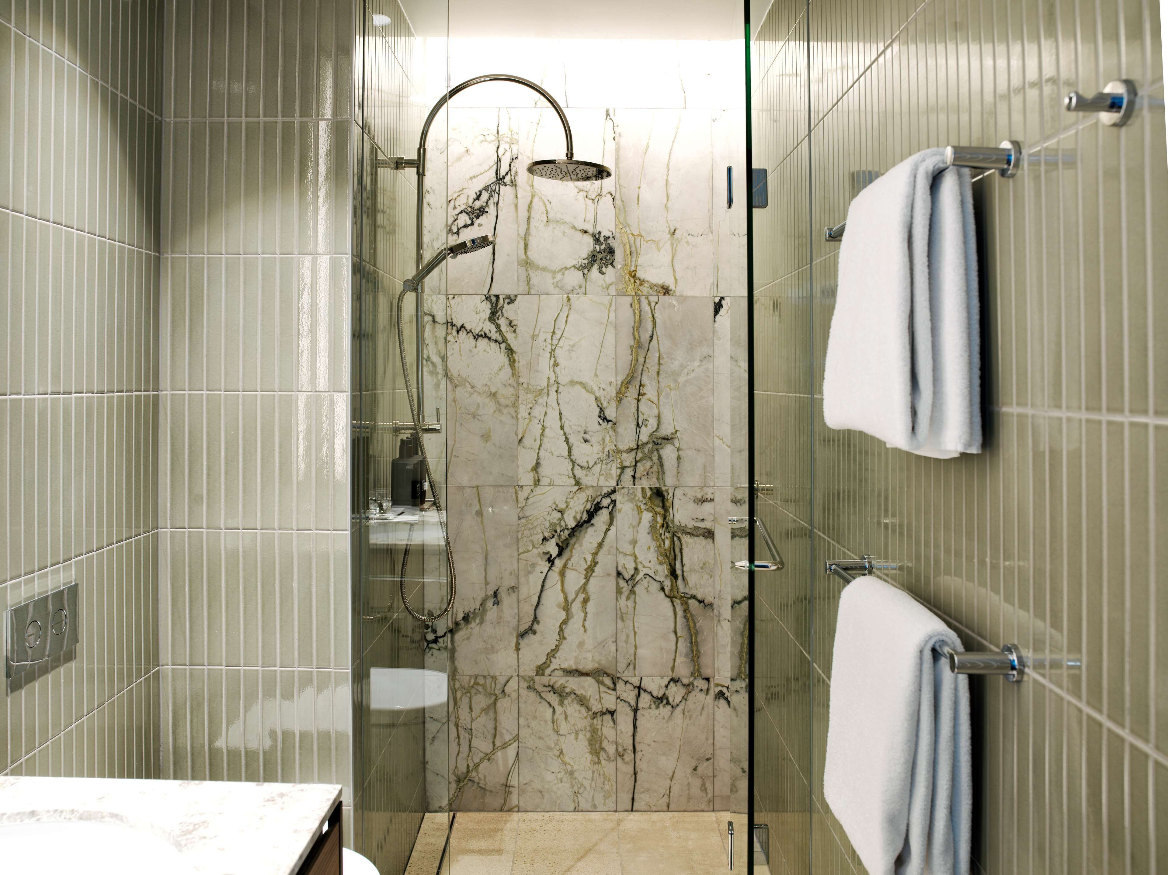 Un baño moderno con ducha de vidrio, paredes de mármol y un perchero para toallas.