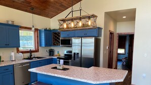 Una cocina moderna con armarios azules, una isla grande con taburetes, electrodomésticos de acero inoxidable y una lámpara colgante original.