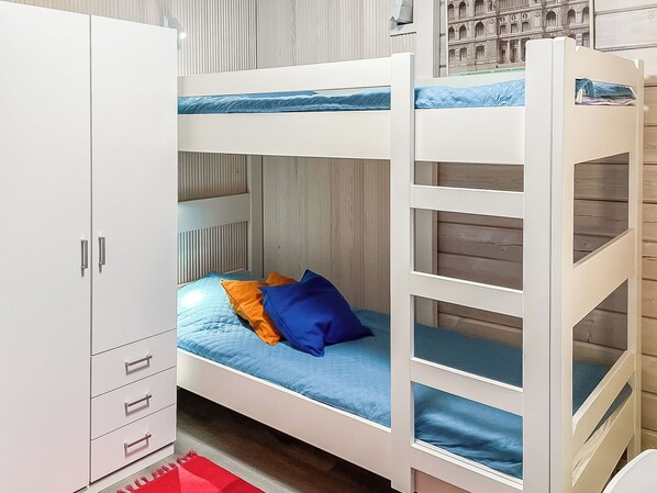 A bunk bed with a lower bunk, a white wardrobe with drawers, and a red rug on the floor.