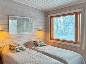 A room with two beds, a framed map on the wall, and a window with a snowy forest view.