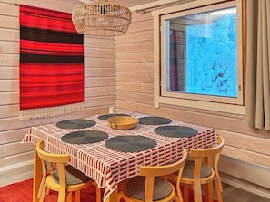 A wooden interior with a table set for four, a red and white patterned tablecloth, and a window with a view of snow.