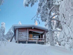 A snow-covered cabin with a wooden exterior, a visible window, and a chimney.