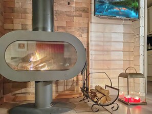 A wood-burning stove with a glass front, a TV mounted on the wall, and a candle holder with lit candles.