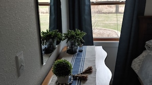 A bedroom with a bed, a bedside table with a potted plant, a mirror, and a window with curtains.