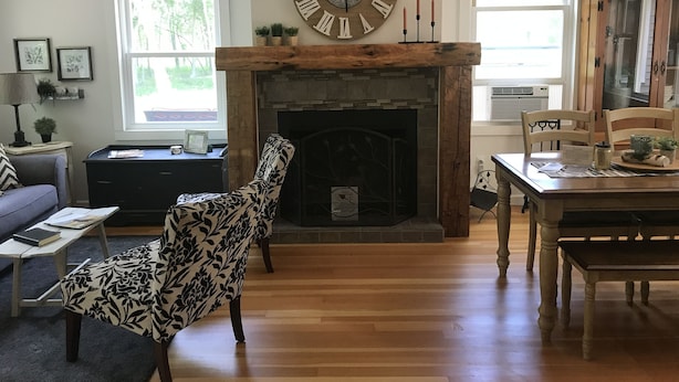 A living room with a fireplace, a large clock, and a dining area with wooden furniture.
