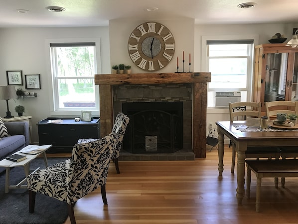 A living room with a fireplace, a large clock, and a dining area with wooden furniture.