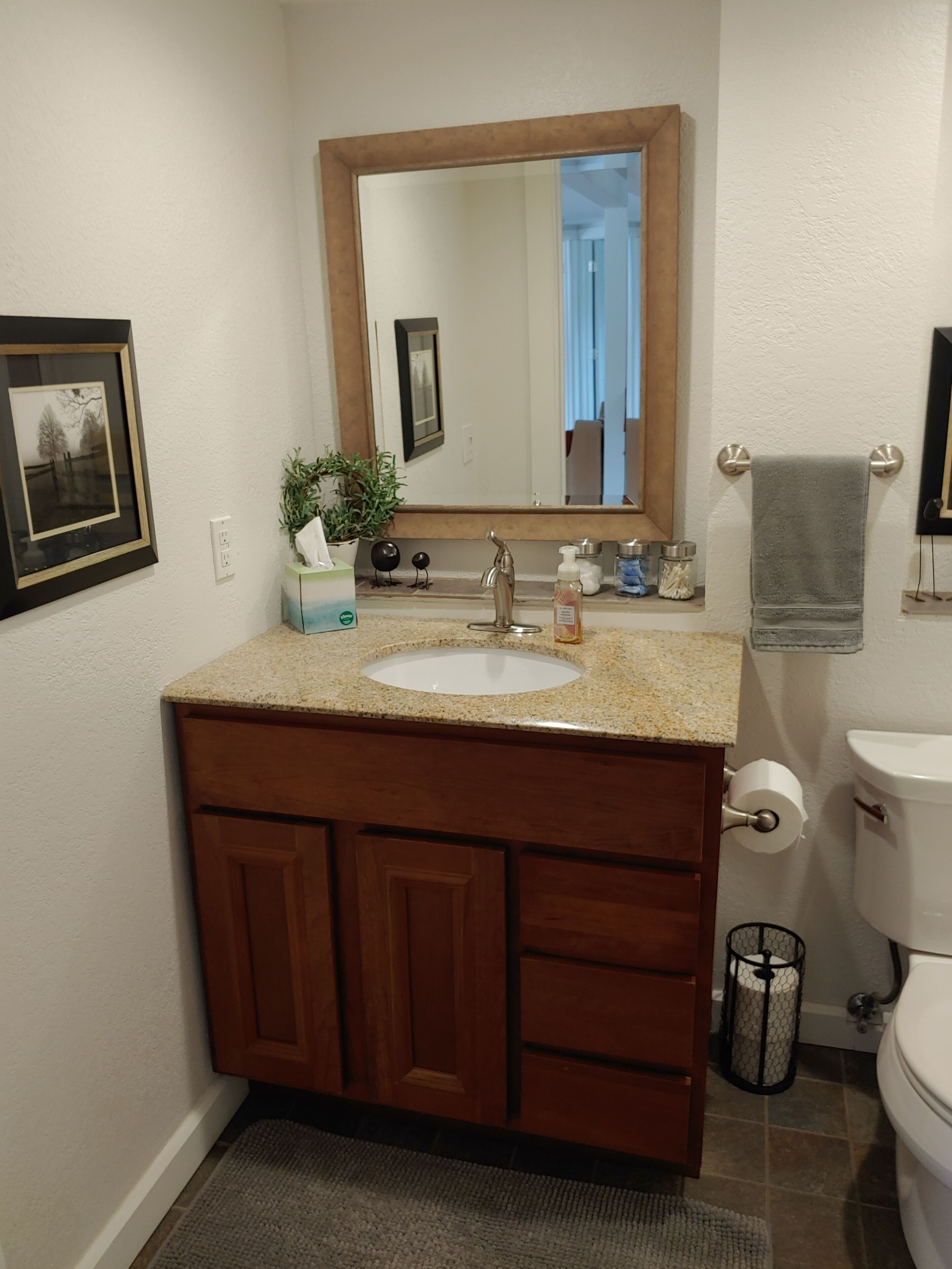 Un baño con tocador de madera, lavamanos, espejo, inodoro y un cubo de basura pequeño.