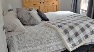 Ein Schlafzimmer mit einem Bett, Kissen, einer gemusterten Tagesdecke, einem Holzschrank und einem Fenster mit Vorhängen.