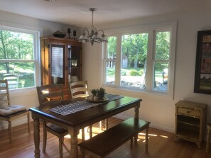A dining area with a wooden table, chairs, and a bench. There is a chandelier above the table, and a cabinet with glass doors is visible. - Tranquil Cottage in the Woods with Lake Michigan only 300 feet away. (Oostburg)