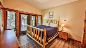 A bedroom with a wooden bed, a nightstand, a lamp, and a window with a view of trees.