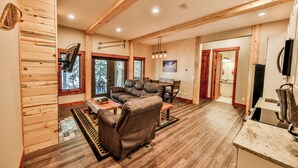 A spacious living room with a leather sofa, wooden beams, and a stone fireplace.