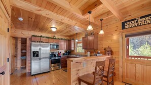 Interieur van een houten blokhut met een keuken, houten balken in het plafond en een bordje met de tekst 'The Great Smoky Mountain'.