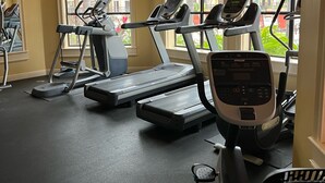 Une salle de sport équipée de tapis de course, de vélos elliptiques et d’un ventilateur de plafond.