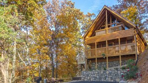 A wooden cabin with a stone foundation, a balcony, and surrounded by autumn trees.