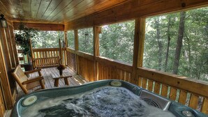 A wooden deck with a hot tub, wooden benches, and a view of a forest.